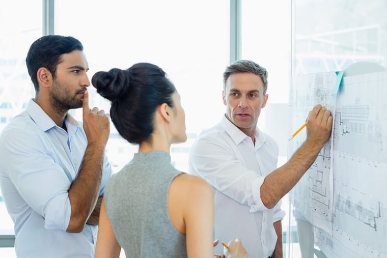 Three engineers reviewing a schematic at a whiteboard